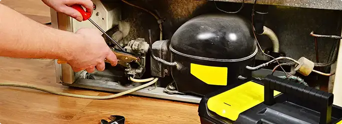 Refrigerator repair technician fixing the compressor and wiring in Wilmington, NC